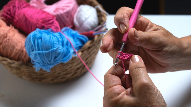 person crocheting with basket of multiple colored balls of yarn