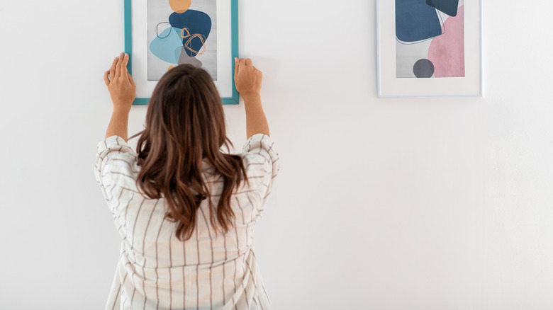 A woman hangs a modern art frame on a wall