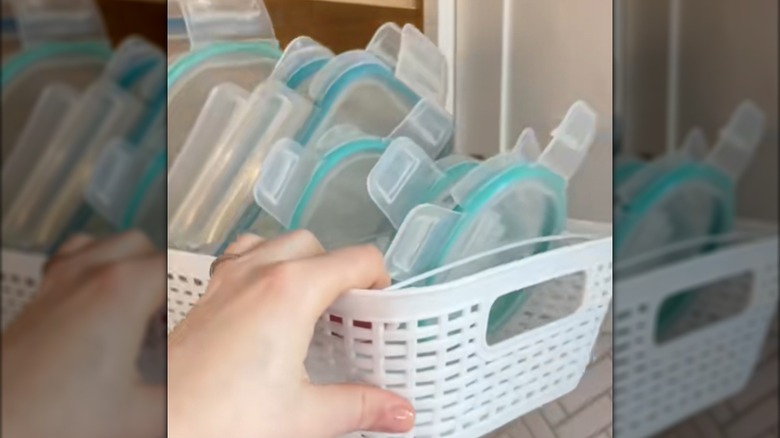 A woman's hand grabs a white basket organizer filled with plastic lids.