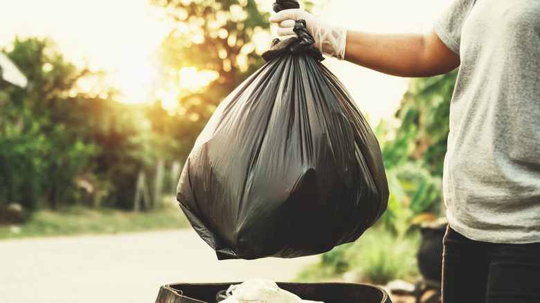 Hand placing full black garbage bag into a trash can