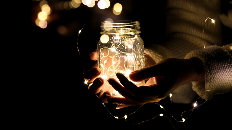 A woman's hands hold a jar with glowing fairy lights in the dark.