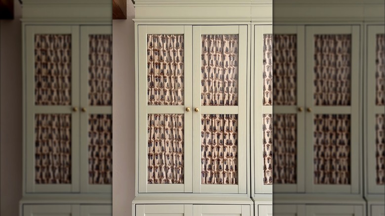 A light green HAVSTA cabinet with pale pink patterned curtains inside the windows.
