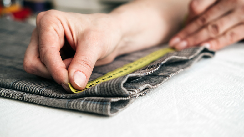 A man measuring grey plaid fabric with measuring tape.