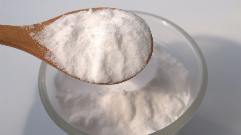 wood spoon filled with baking soda over a glass bowl of baking soda