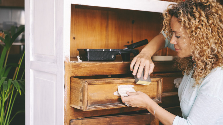 A woman is sanding down cabinets before painting