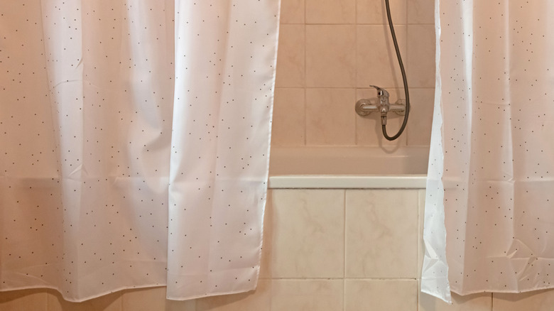 Two shower curtains in front of an older bathroom tub