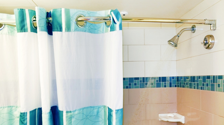 A blue and white shower curtain hangs half-open next to a running showerhead.