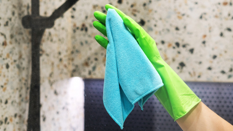 Gloved hand wiping down shower glass with microfiber cloth