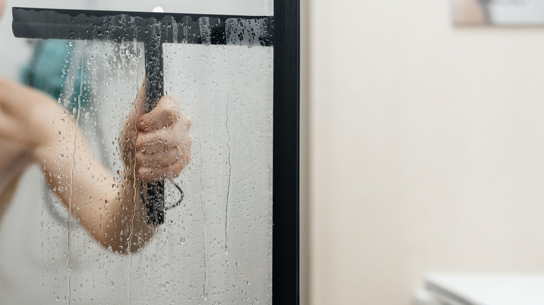 Closeup of hand using a squeegee to clean shower glass