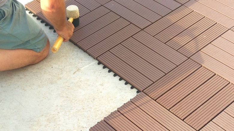 Man installing brown composite decking tiles with soft hammer