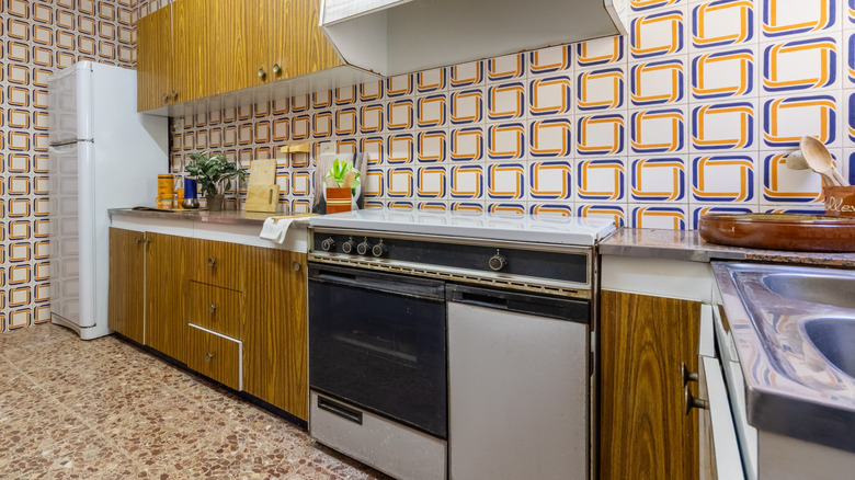 An ugly kitchen with loud, tile-like wallpaper and clashing faux-stone flooring.