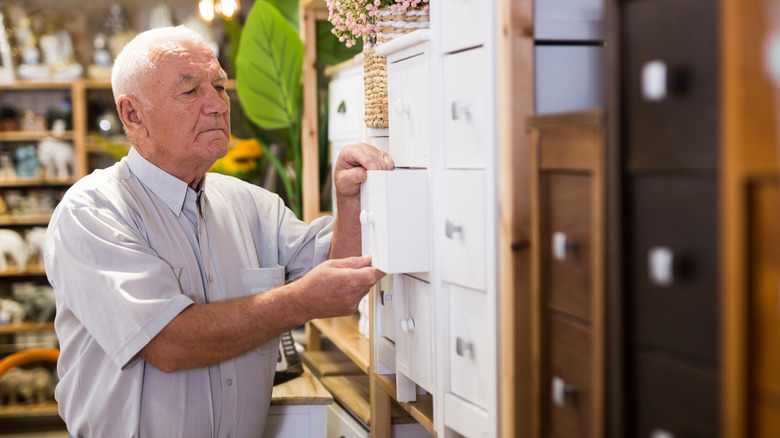 Portrait of elderly man choosing wooden chest of drawers in a furniture store