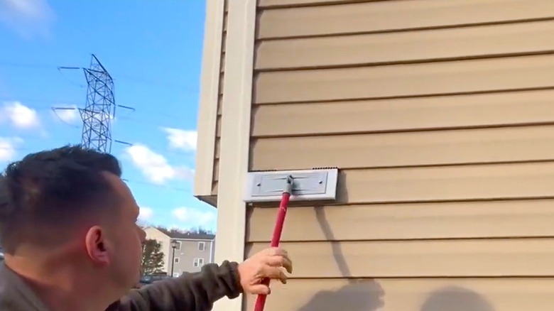 A man using a vinyl siding cleaning brush to clean the siding on his house