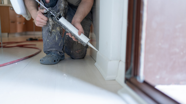 Contractor using a caulking gun along a baseboard