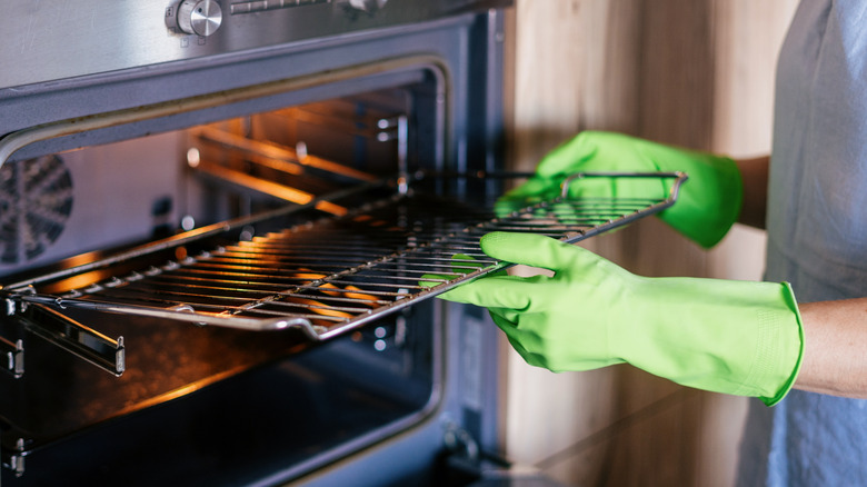 Someone wearing green rubber gloves removing an oven rack