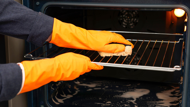 Someone cleaning oven racks with a sponge