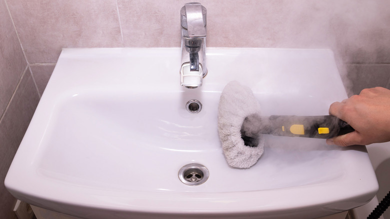 person steam cleaning sink interior