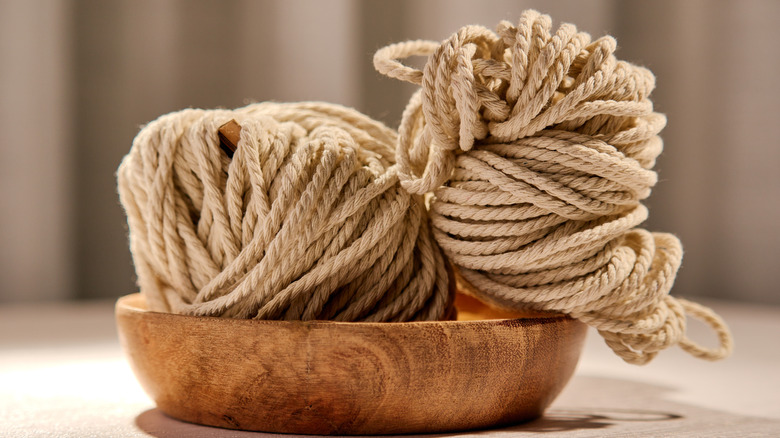 Rolls of jute rope sitting in wooden bowl on table.