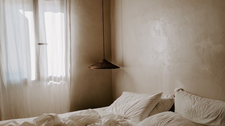 Bedroom with bed, hanging pendant light, and neutral, limewash paint on walls