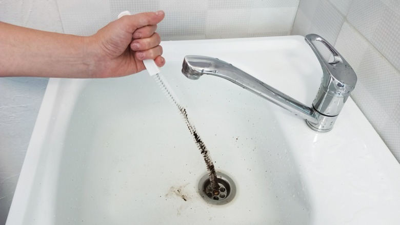 Person cleaning bathroom sink drain with long brush