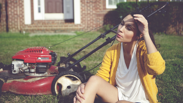 Tired woman sitting by lawnmower