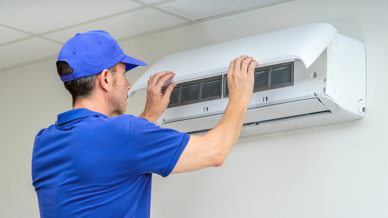 An HVAC technician examines a wall-mounted air conditioner