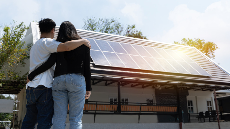 A couple stand outside their home admiring their new solar panels.