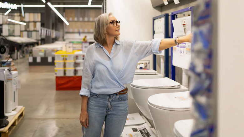 A middle-aged woman shops for toilets at a home improvement store.
