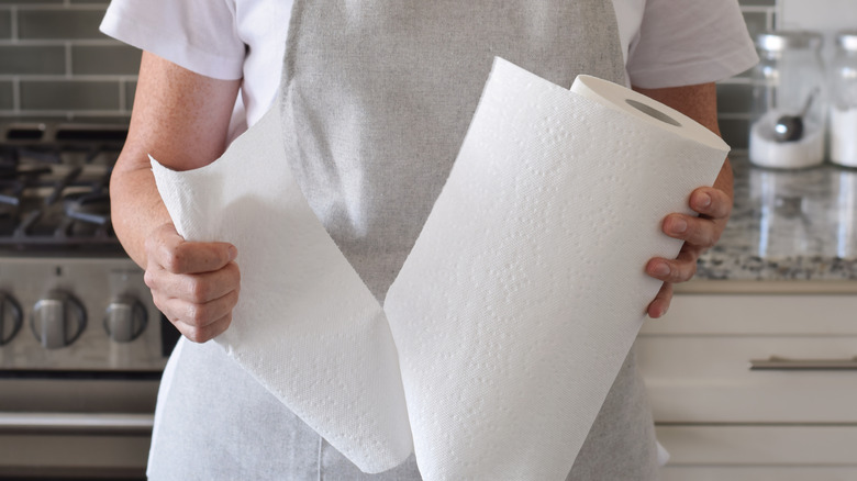 A person wearing a gray apron pulling a paper towel off the roll