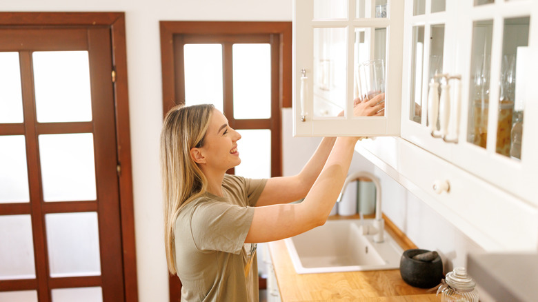 A woman grabbing a glass from a glass-front kitchen cabinet
