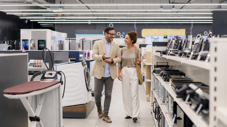 A woman and a man stroll the aisle in an appliance store.