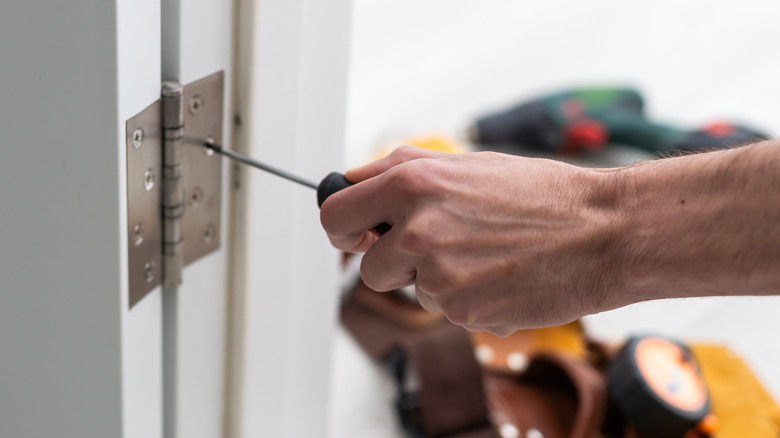 Man unscrewing door hinges with a screwdriver.