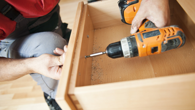A person assembling furniture using a drill.