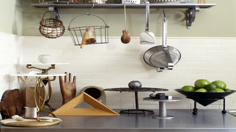 Kitchen wall featuring mounted shelf with items, such as decor, spatulas, and a cooking pan, maximizing storage space.
