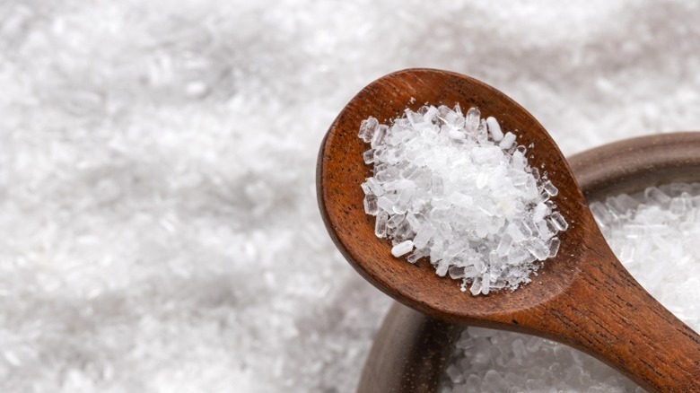 Wooden spoon with Epsom salt crystals in a wooden bowl, surrounded by more salt crystals.