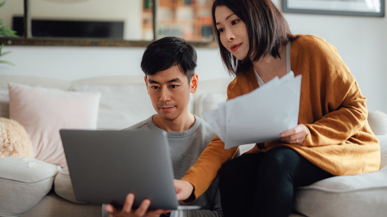 Asian couple looking over paperwork and a tablet in a living room setting