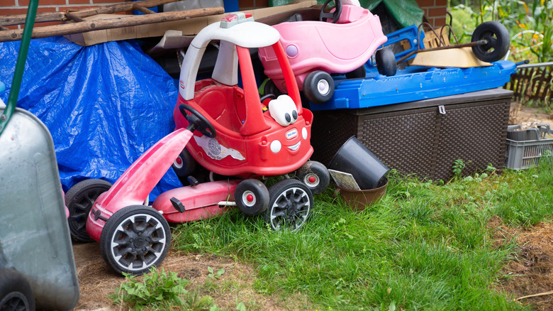 Lawn clutter including a Little Tikes car and other children's vehicles near the side of a house