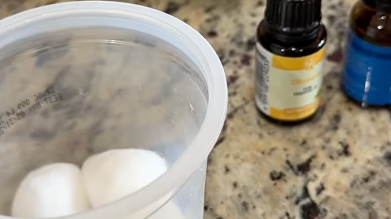 A container with cotton balls next to essential oil.