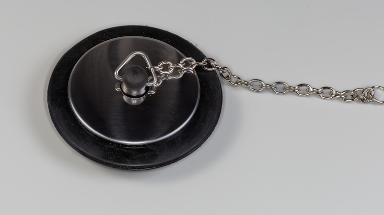 A closeup image of a black rubber and metal drain stopper with a chain