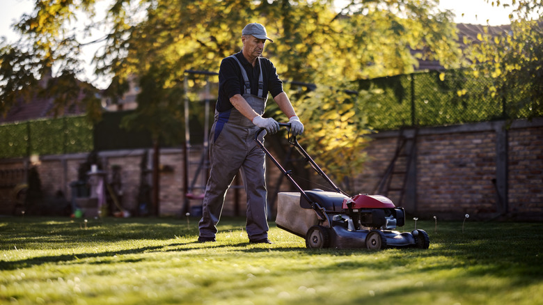 A professional work person in overalls mows the lawn in a client's backyard.
