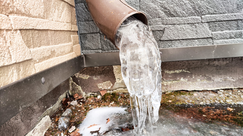 A gutter downspout filled up with ice at the corner of a home with lots of ice underneath