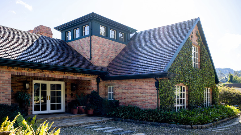 A brick home with a dark roof, white trim, and climbing vines on the front.