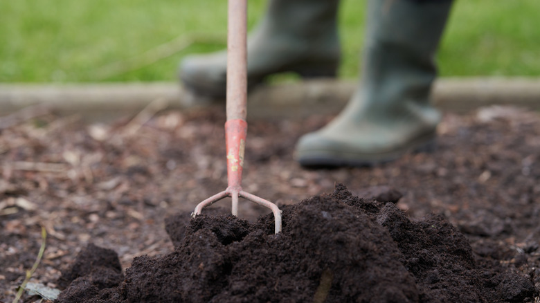 A mound of compost with a hoe sticking out and a gardener's boots in the background