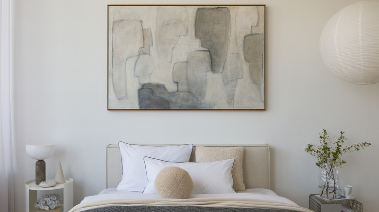 A large piece of art hangs on the wall over a bed.