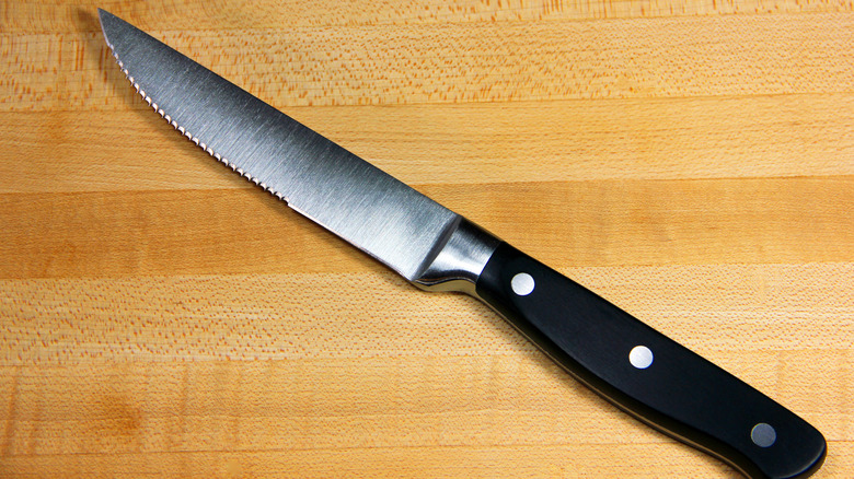 A steak knife placed on a wooden cutting board