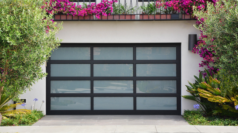 A contemporary garage door is surrounded by pink flowers and lush landscaping