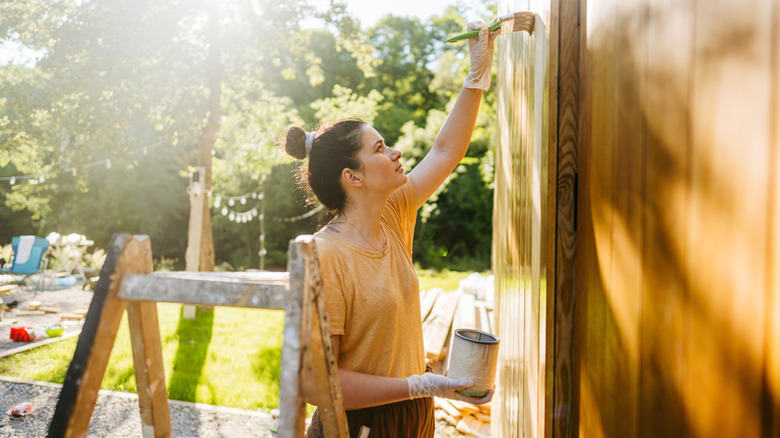 Woman painting or staining wood exterior wall.