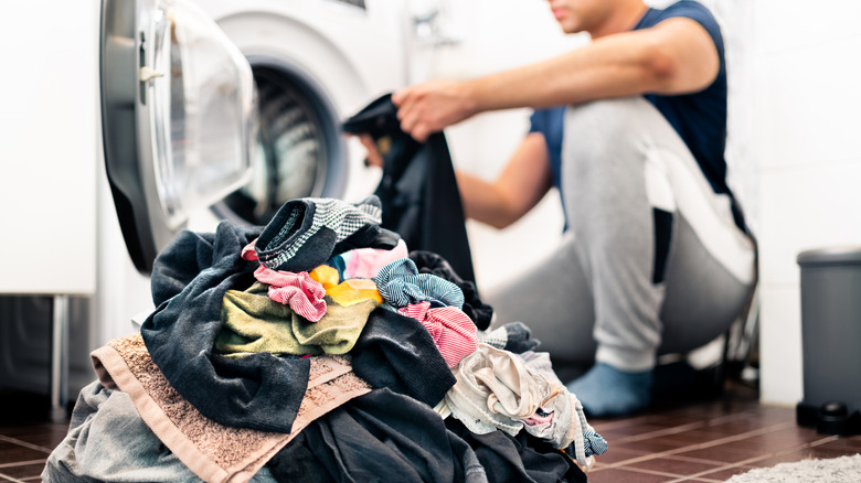 Man loading washer machine and sorting by color and fabric.
