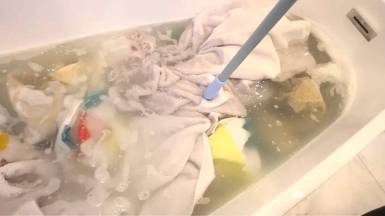 Laundry soaks in a bathtub full of water and cleaning products.