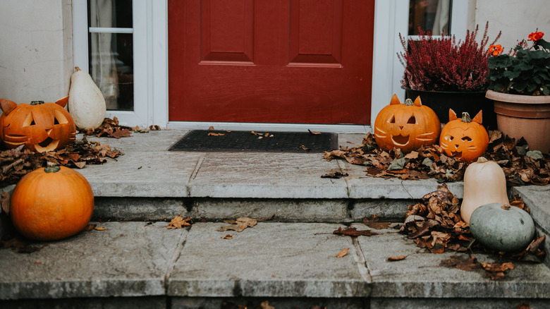 A front porch with a red door is decorated with carved and whole pumpkins and fall leaves.